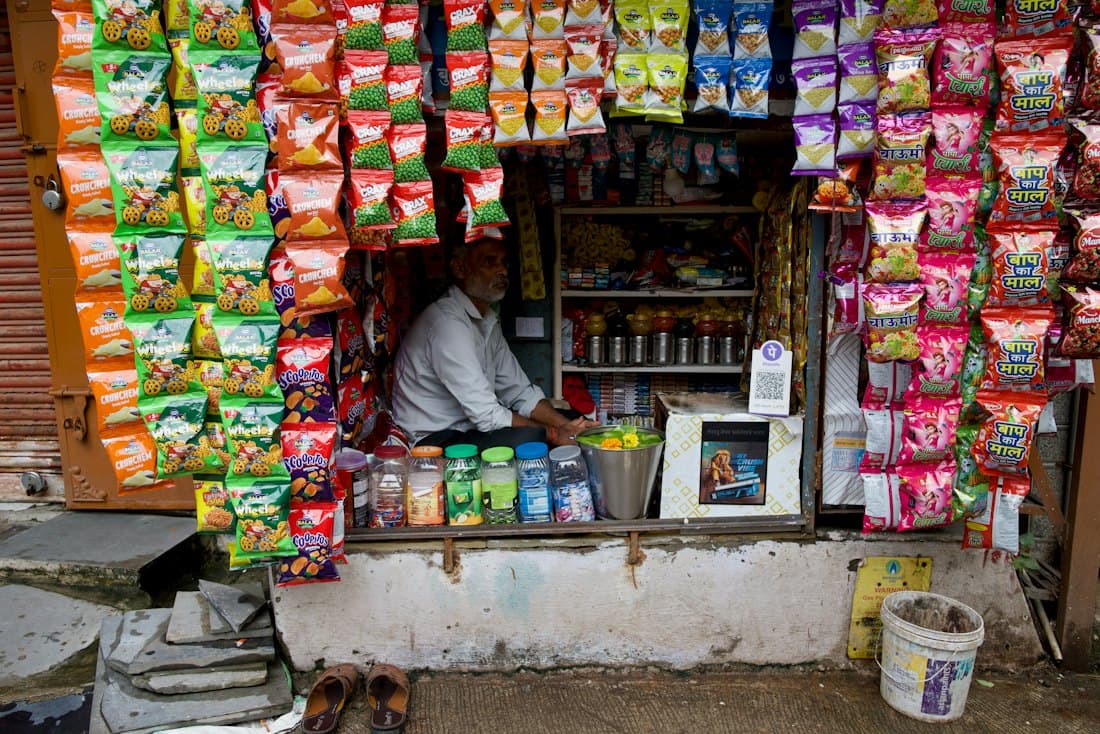 Shopkeeper at a small store counter lined with snacks and drinks