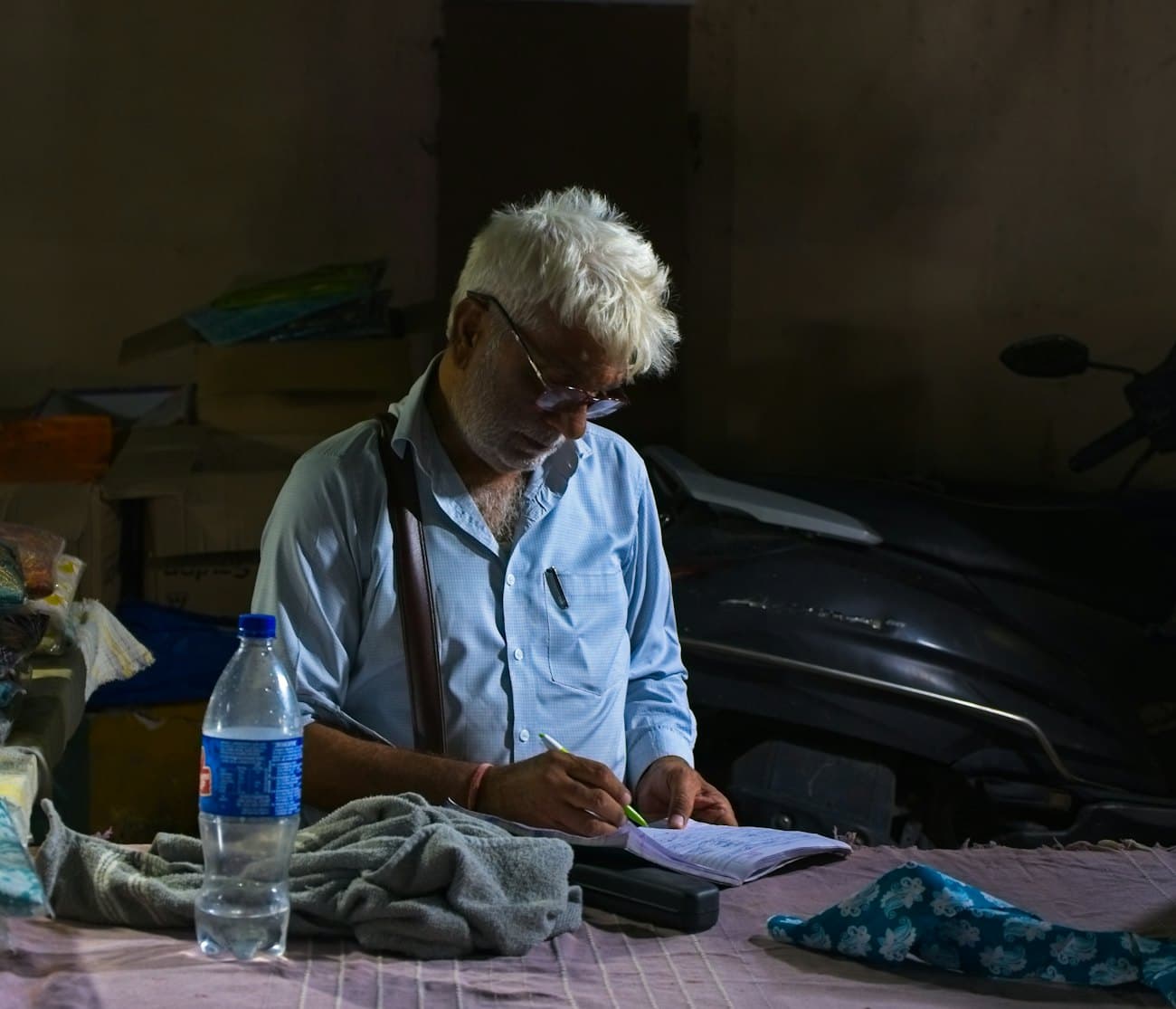 Elderly shop owner writing accounts by hand in a register